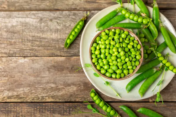 Ahşap zemin üzerinde yeşil bezelyeler olan taze bezelye kabukları. Tatlı yeşil bezelyeler. Yeşil bezelye fasulyesi sebzesi. Vejetaryen. Sağlıklı sebze. Boşluğu kopyala