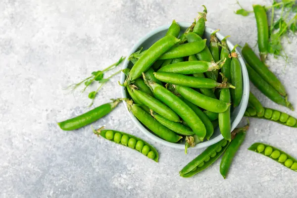 Ahşap zemin üzerinde yeşil bezelyeler olan taze bezelye kabukları. Tatlı yeşil bezelyeler. Yeşil bezelye fasulyesi sebzesi. Vejetaryen. Sağlıklı sebze. Boşluğu kopyala