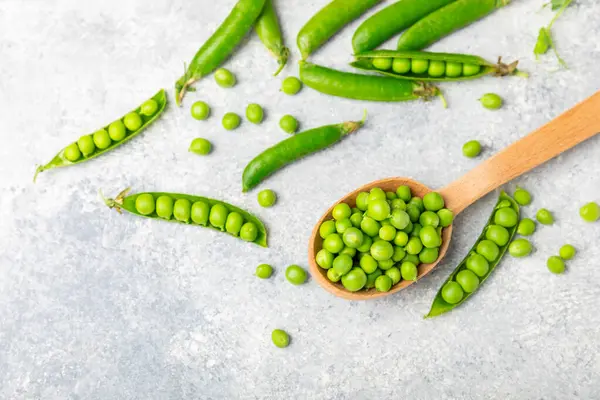 Ahşap zemin üzerinde yeşil bezelyeler olan taze bezelye kabukları. Tatlı yeşil bezelyeler. Yeşil bezelye fasulyesi sebzesi. Vejetaryen. Sağlıklı sebze. Boşluğu kopyala