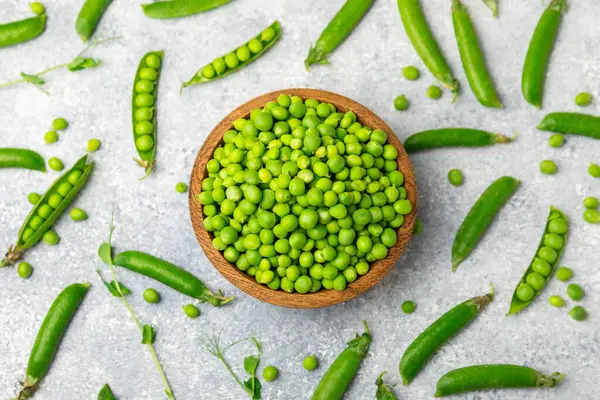 Ahşap zemin üzerinde yeşil bezelyeler olan taze bezelye kabukları. Tatlı yeşil bezelyeler. Yeşil bezelye fasulyesi sebzesi. Vejetaryen. Sağlıklı sebze. Boşluğu kopyala