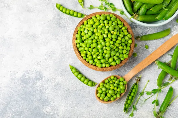 Ahşap zemin üzerinde yeşil bezelyeler olan taze bezelye kabukları. Tatlı yeşil bezelyeler. Yeşil bezelye fasulyesi sebzesi. Vejetaryen. Sağlıklı sebze. Boşluğu kopyala