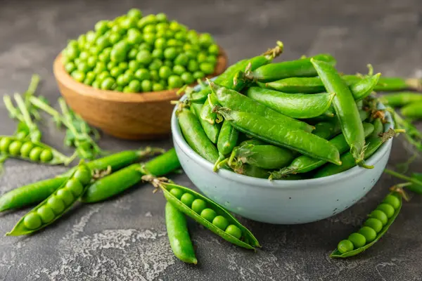 Ahşap zemin üzerinde yeşil bezelyeler olan taze bezelye kabukları. Tatlı yeşil bezelyeler. Yeşil bezelye fasulyesi sebzesi. Vejetaryen. Sağlıklı sebze. Boşluğu kopyala