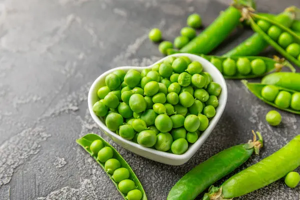 Ahşap zemin üzerinde yeşil bezelyeler olan taze bezelye kabukları. Tatlı yeşil bezelyeler. Yeşil bezelye fasulyesi sebzesi. Vejetaryen. Sağlıklı sebze. Boşluğu kopyala