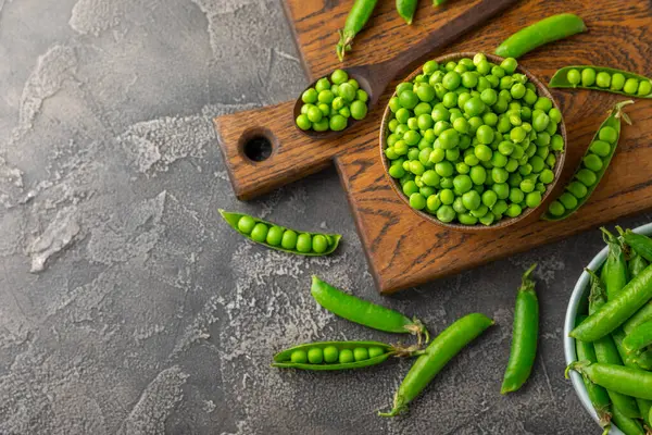 Ahşap zemin üzerinde yeşil bezelyeler olan taze bezelye kabukları. Tatlı yeşil bezelyeler. Yeşil bezelye fasulyesi sebzesi. Vejetaryen. Sağlıklı sebze. Boşluğu kopyala