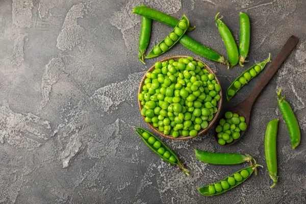 Ahşap zemin üzerinde yeşil bezelyeler olan taze bezelye kabukları. Tatlı yeşil bezelyeler. Yeşil bezelye fasulyesi sebzesi. Vejetaryen. Sağlıklı sebze. Boşluğu kopyala