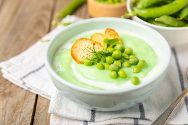 Ahşap bir masada yeşil bezelye çorbası. Taze bezelye çorbası kasesi. Yeşil bezelye ve kızarmış ekmekle dolu bir kasede lezzetli, sağlıklı krema çorbası. Sağlıklı vejetaryen püresi. Uzayı kopyala Metin için boşluk.