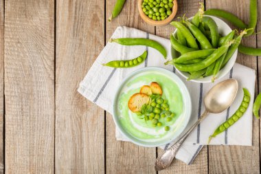 Ahşap bir masada yeşil bezelye çorbası. Taze bezelye çorbası kasesi. Yeşil bezelye ve kızarmış ekmekle dolu bir kasede lezzetli, sağlıklı krema çorbası. Sağlıklı vejetaryen püresi. Uzayı kopyala Metin için boşluk.