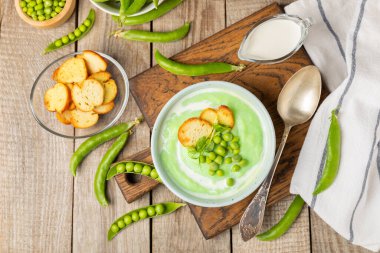 Ahşap bir masada yeşil bezelye çorbası. Taze bezelye çorbası kasesi. Yeşil bezelye ve kızarmış ekmekle dolu bir kasede lezzetli, sağlıklı krema çorbası. Sağlıklı vejetaryen püresi. Uzayı kopyala Metin için boşluk.