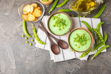 Ahşap bir masada yeşil bezelye çorbası. Taze bezelye çorbası kasesi. Yeşil bezelye ve kızarmış ekmekle dolu bir kasede lezzetli, sağlıklı krema çorbası. Sağlıklı vejetaryen püresi. Uzayı kopyala Metin için boşluk.