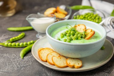 Ahşap bir masada yeşil bezelye çorbası. Taze bezelye çorbası kasesi. Yeşil bezelye ve kızarmış ekmekle dolu bir kasede lezzetli, sağlıklı krema çorbası. Sağlıklı vejetaryen püresi. Uzayı kopyala Metin için boşluk.