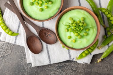 Ahşap bir masada yeşil bezelye çorbası. Taze bezelye çorbası kasesi. Yeşil bezelye ve kızarmış ekmekle dolu bir kasede lezzetli, sağlıklı krema çorbası. Sağlıklı vejetaryen püresi. Uzayı kopyala Metin için boşluk.