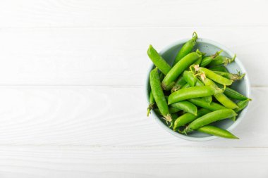 Ahşap zemin üzerinde yeşil bezelyeler olan taze bezelye kabukları. Tatlı yeşil bezelyeler. Yeşil bezelye fasulyesi sebzesi. Vejetaryen. Sağlıklı sebze. Boşluğu kopyala