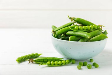 Ahşap zemin üzerinde yeşil bezelyeler olan taze bezelye kabukları. Tatlı yeşil bezelyeler. Yeşil bezelye fasulyesi sebzesi. Vejetaryen. Sağlıklı sebze. Boşluğu kopyala