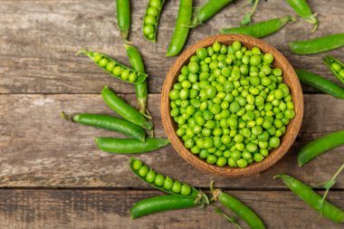 Ahşap zemin üzerinde yeşil bezelyeler olan taze bezelye kabukları. Tatlı yeşil bezelyeler. Yeşil bezelye fasulyesi sebzesi. Vejetaryen. Sağlıklı sebze. Boşluğu kopyala