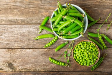 Ahşap zemin üzerinde yeşil bezelyeler olan taze bezelye kabukları. Tatlı yeşil bezelyeler. Yeşil bezelye fasulyesi sebzesi. Vejetaryen. Sağlıklı sebze. Boşluğu kopyala