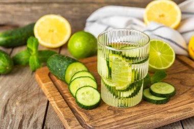 Salatalık suyu, limon, nane ve ahşap bir masada. İçme bardağında dilimlenmiş salatalık ile karıştırılmış su. Tonik ferahlatıcı bir içecek. Salatalık limonata. Doğal soğutma içeceği. Boşluğu kopyala.