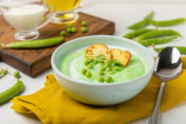Ahşap bir masada yeşil bezelye çorbası. Taze bezelye çorbası kasesi. Yeşil bezelye ve kızarmış ekmekle dolu bir kasede lezzetli, sağlıklı krema çorbası. Sağlıklı vejetaryen püresi. Uzayı kopyala Metin için boşluk.
