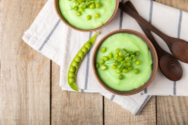 Ahşap bir masada yeşil bezelye çorbası. Taze bezelye çorbası kasesi. Yeşil bezelye ve kızarmış ekmekle dolu bir kasede lezzetli, sağlıklı krema çorbası. Sağlıklı vejetaryen püresi. Uzayı kopyala Metin için boşluk.