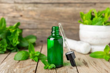 Ahşap bir arka planda esaslı bir nane şekeri. Naneli esaslı yağ ve taze nane yaprakları. Bir şişe aromaterapi yağı. Nane özütü. Doğal kozmetik konsepti, spa bakımı. Boşluğu kopyala