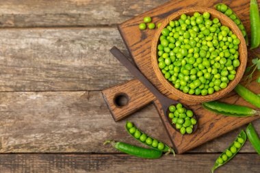 Ahşap zemin üzerinde yeşil bezelyeler olan taze bezelye kabukları. Tatlı yeşil bezelyeler. Yeşil bezelye fasulyesi sebzesi. Vejetaryen. Sağlıklı sebze. Boşluğu kopyala