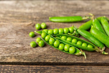 Ahşap zemin üzerinde yeşil bezelyeler olan taze bezelye kabukları. Tatlı yeşil bezelyeler. Yeşil bezelye fasulyesi sebzesi. Vejetaryen. Sağlıklı sebze. Boşluğu kopyala