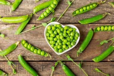 Ahşap zemin üzerinde yeşil bezelyeler olan taze bezelye kabukları. Tatlı yeşil bezelyeler. Yeşil bezelye fasulyesi sebzesi. Vejetaryen. Sağlıklı sebze. Boşluğu kopyala