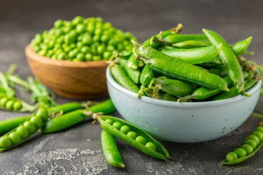 Ahşap zemin üzerinde yeşil bezelyeler olan taze bezelye kabukları. Tatlı yeşil bezelyeler. Yeşil bezelye fasulyesi sebzesi. Vejetaryen. Sağlıklı sebze. Boşluğu kopyala