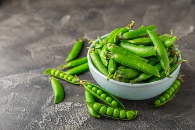 Ahşap zemin üzerinde yeşil bezelyeler olan taze bezelye kabukları. Tatlı yeşil bezelyeler. Yeşil bezelye fasulyesi sebzesi. Vejetaryen. Sağlıklı sebze. Boşluğu kopyala