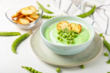 Ahşap bir masada yeşil bezelye çorbası. Taze bezelye çorbası kasesi. Yeşil bezelye ve kızarmış ekmekle dolu bir kasede lezzetli, sağlıklı krema çorbası. Sağlıklı vejetaryen püresi. Uzayı kopyala Metin için boşluk.