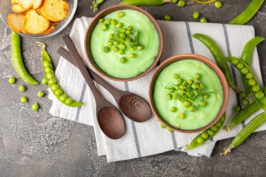 Ahşap bir masada yeşil bezelye çorbası. Taze bezelye çorbası kasesi. Yeşil bezelye ve kızarmış ekmekle dolu bir kasede lezzetli, sağlıklı krema çorbası. Sağlıklı vejetaryen püresi. Uzayı kopyala Metin için boşluk.