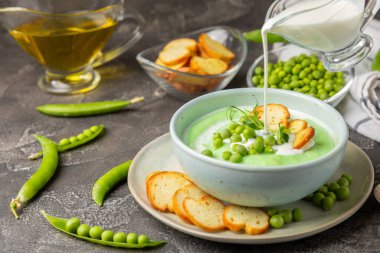 Ahşap bir masada yeşil bezelye çorbası. Taze bezelye çorbası kasesi. Yeşil bezelye ve kızarmış ekmekle dolu bir kasede lezzetli, sağlıklı krema çorbası. Sağlıklı vejetaryen püresi. Uzayı kopyala Metin için boşluk.