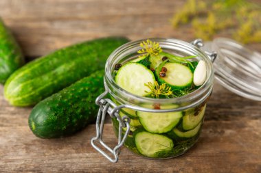 Ahşap bir arka planda kavanozda taze tuzlanmış ev yapımı salatalıklar. Dereotlu, sarımsaklı ve biberli salatalık turşusu. Konserve salatalık, salatalık ve penis. Ev yapımı koruma..