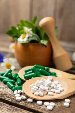 Ahşap zemin üzerinde alternatif ilaç bitkisel kapsül organik ilaç. Bitki ve tablet çeşitleri, vitaminler ve diyet takviyeleri. Sağlıklı yaşam için tıbbi ve şifalı bitkiler.