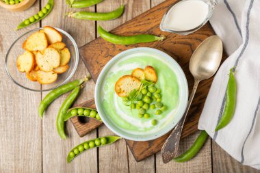 Ahşap bir masada yeşil bezelye çorbası. Taze bezelye çorbası kasesi. Yeşil bezelye ve kızarmış ekmekle dolu bir kasede lezzetli, sağlıklı krema çorbası. Sağlıklı vejetaryen püresi. Uzayı kopyala Metin için boşluk.