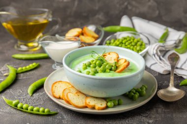 Ahşap bir masada yeşil bezelye çorbası. Taze bezelye çorbası kasesi. Yeşil bezelye ve kızarmış ekmekle dolu bir kasede lezzetli, sağlıklı krema çorbası. Sağlıklı vejetaryen püresi. Uzayı kopyala Metin için boşluk.