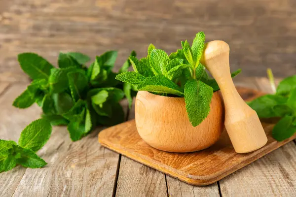 Ahşap zemin üzerinde havan ve kabuk ile taze nane. Melissa gider. Şifalı bitkiler, ilaç için havanda yeşil nane yaprakları. Mesaj için alan. Boşluğu kopyala.