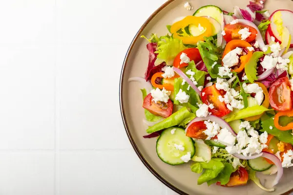 Ahşap bir arka planda salatalık. Taze sebzeli, salatalıklı, domatesli, tatlı biberli ve salatalı ev yapımı salata. Vejetaryen bahar salatası.