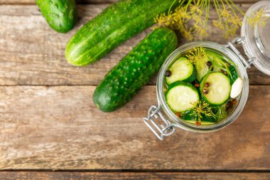 Ahşap bir arka planda kavanozda taze tuzlanmış ev yapımı salatalıklar. Dereotlu, sarımsaklı ve biberli salatalık turşusu. Konserve salatalık, salatalık ve penis. Ev yapımı koruma..