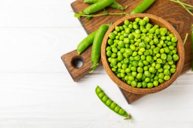 Ahşap zemin üzerinde yeşil bezelyeler olan taze bezelye kabukları. Tatlı yeşil bezelyeler. Yeşil bezelye fasulyesi sebzesi. Vejetaryen. Sağlıklı sebze. Boşluğu kopyala