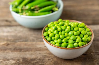 Ahşap zemin üzerinde yeşil bezelyeler olan taze bezelye kabukları. Tatlı yeşil bezelyeler. Yeşil bezelye fasulyesi sebzesi. Vejetaryen. Sağlıklı sebze. Boşluğu kopyala