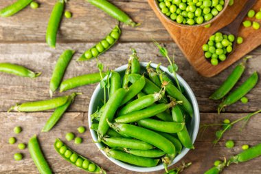 Ahşap zemin üzerinde yeşil bezelyeler olan taze bezelye kabukları. Tatlı yeşil bezelyeler. Yeşil bezelye fasulyesi sebzesi. Vejetaryen. Sağlıklı sebze. Boşluğu kopyala