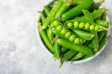 Ahşap zemin üzerinde yeşil bezelyeler olan taze bezelye kabukları. Tatlı yeşil bezelyeler. Yeşil bezelye fasulyesi sebzesi. Vejetaryen. Sağlıklı sebze. Boşluğu kopyala