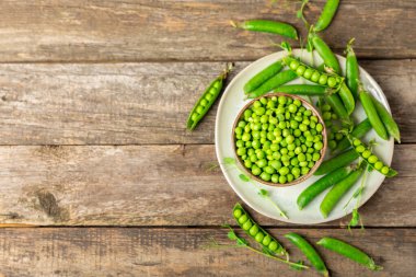 Ahşap zemin üzerinde yeşil bezelyeler olan taze bezelye kabukları. Tatlı yeşil bezelyeler. Yeşil bezelye fasulyesi sebzesi. Vejetaryen. Sağlıklı sebze. Boşluğu kopyala
