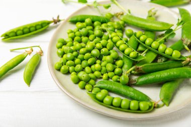 Ahşap zemin üzerinde yeşil bezelyeler olan taze bezelye kabukları. Tatlı yeşil bezelyeler. Yeşil bezelye fasulyesi sebzesi. Vejetaryen. Sağlıklı sebze. Boşluğu kopyala