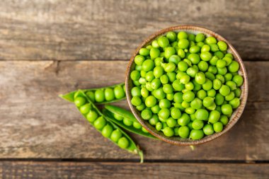 Ahşap zemin üzerinde yeşil bezelyeler olan taze bezelye kabukları. Tatlı yeşil bezelyeler. Yeşil bezelye fasulyesi sebzesi. Vejetaryen. Sağlıklı sebze. Boşluğu kopyala