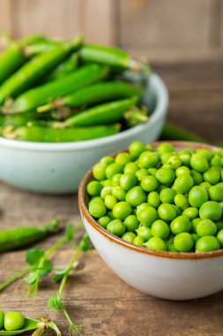Ahşap zemin üzerinde yeşil bezelyeler olan taze bezelye kabukları. Tatlı yeşil bezelyeler. Yeşil bezelye fasulyesi sebzesi. Vejetaryen. Sağlıklı sebze. Boşluğu kopyala