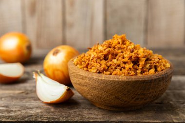 Tahta bir masada kasede kızarmış soğan. Kızarmış soğan. Bulaşık çeşnisi. Baharatlar. Salata sosu. Mesaj için yer var. Boşluğu kopyala