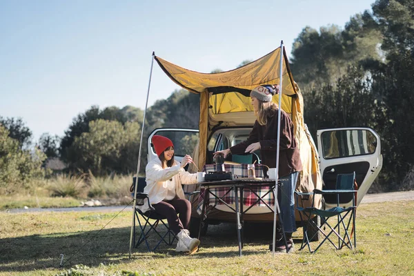 Couple preparing coffee in their van. Women enjoying a day camping. Winter vacations and relationship concept.