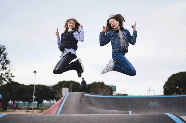 Teenage blonde sisters jumping on a pump track park doing the victory symbol. Concept of fun and health.