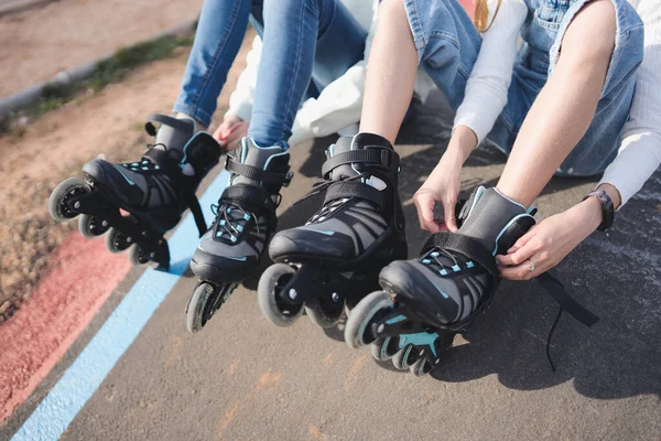 Close-up of two sisters putting on inline skates in a pump track park.